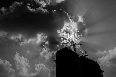Industrial construction cranes silhouette over sunrise. Processed in black and white.