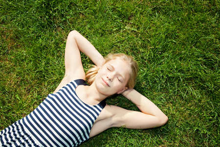 little girl lying on green grassの写真素材