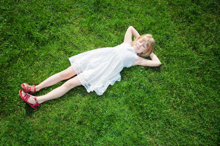 little girl lying on green grassの写真素材