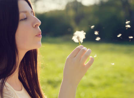 young woman blowing on a white dandelionの写真素材