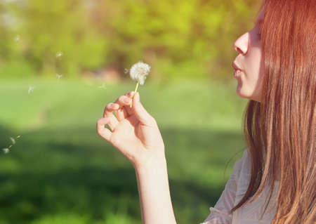 young woman blowing on a white dandelionの写真素材