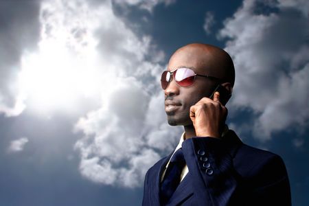 black businessman talking at mobile against a sunny skyの写真素材
