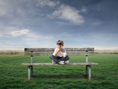 Smiling child sitting on a park bench with green meadow in the backgroundの写真素材