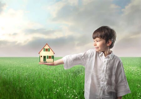 Smiling child on a green meadow holding the model of a houseの写真素材