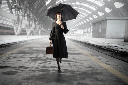 Beautiful woman with umbrella standing on the platform of a train stationの写真素材