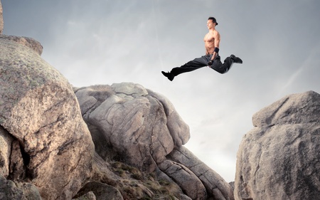 Handsome brawny man jumping from a rock to another