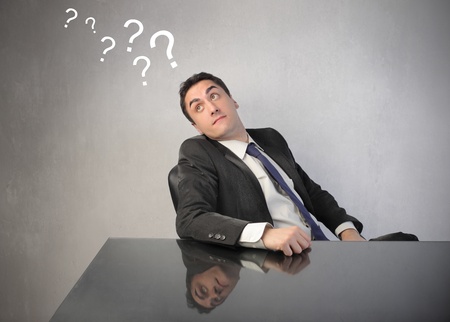 Doubtful businessman with question marks over his headの写真素材