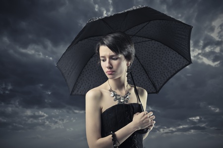 Sad elegant woman under an umbrella with stormy sky in the backgroundの写真素材