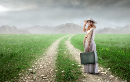 Elegant woman carrying a suitcase on a countryside roadの写真素材