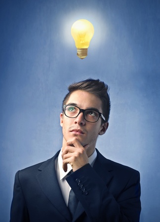 Young businessman with thoughtful expression and light bulb over his headの写真素材