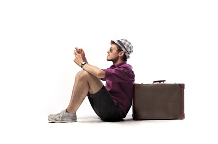 Young tourist sitting against a suitcase and using a mobile phone