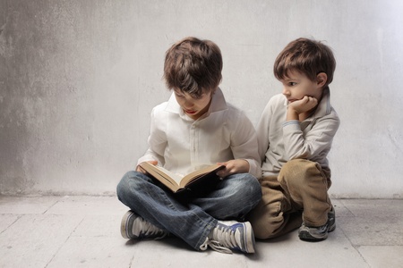 Child reading a book and little brother observing himの写真素材