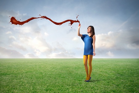 Smiling beautiful woman filling the air with red paint on a green meadow