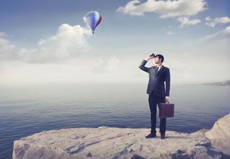 Businessman using binoculars with seascape and hot-air balloon in the backgroundの写真素材
