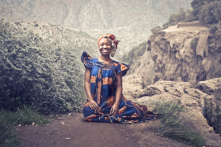 Smiling african woman in traditional dress sitting on a rockの写真素材