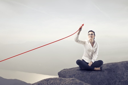Smiling businesswoman sitting on a rock over a lake and charting a positive trend graphの写真素材