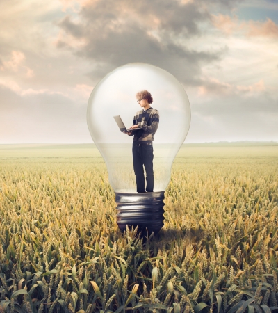 Young man in a light bulb on a wheat field using a laptopの写真素材
