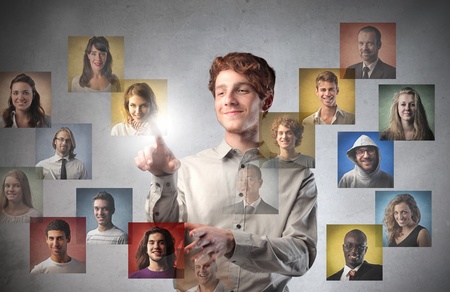 Smiling young man touching icons of different people on a touchscreenの写真素材