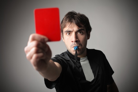 Angry referee whistling and raising a red cardの写真素材