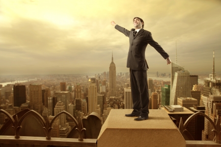 Businessman on a skyscraper stretching out his arms with big city in the backgroundの写真素材