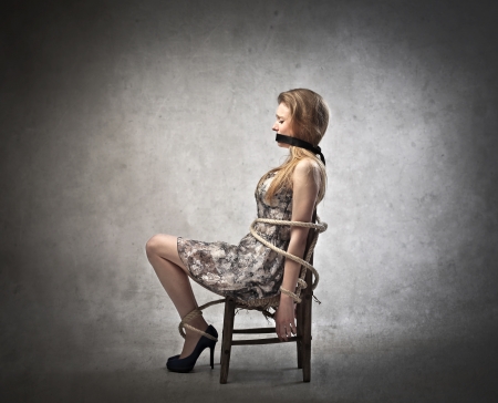 Sad scared young woman tied tight to a chairの写真素材