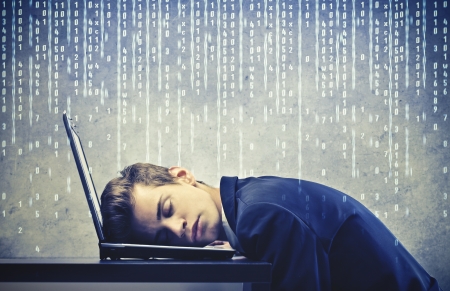 Young businessman sleeping on his laptop computer with some computer codes on the backgroundの写真素材