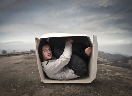 Man crouched into a box in a wasteland