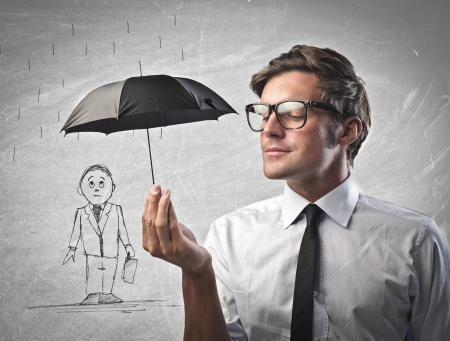 Businessman protecting  with a black umbrella another businessman drawn on a white a wallの写真素材