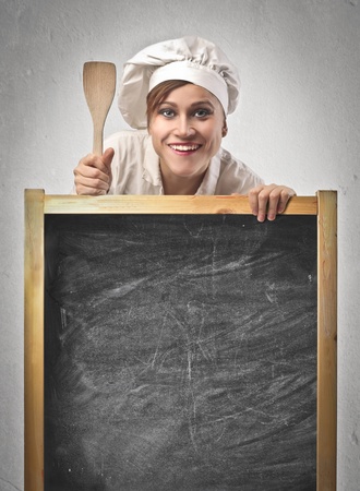 Woman cook over a blackboard with a wooden spoonの写真素材