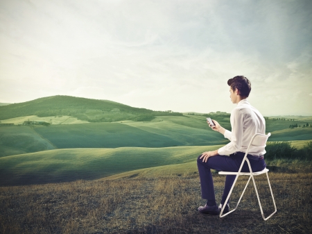 young businessman sitting with telephone in hand in beautiful landscapeの写真素材