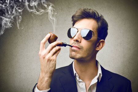 man wearing sunglasses and smoking a pipeの写真素材