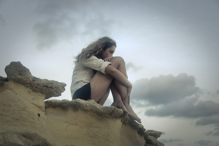 Lonely girl sitting on a rockの写真素材