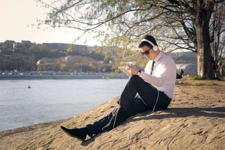 Businessman by the river listening to musicの写真素材