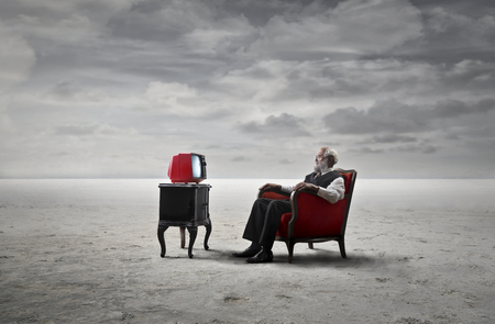 Old man is watching the tv in the desertの写真素材