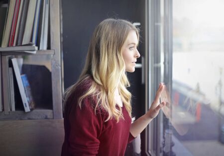 Blonde girl is watching through the windowの写真素材