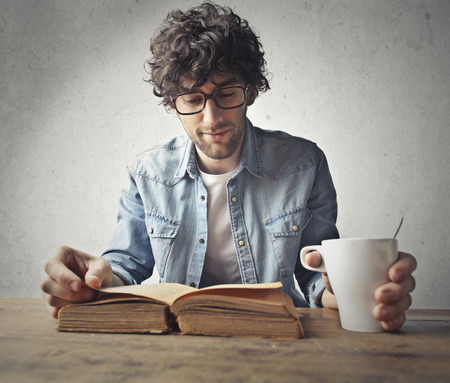 Boy is reading a big book and drinking a coffeeの写真素材