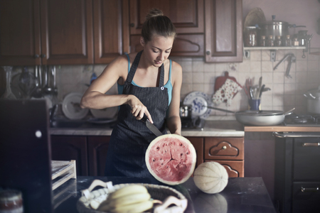 Girl opening watermelon in a kitchenの写真素材