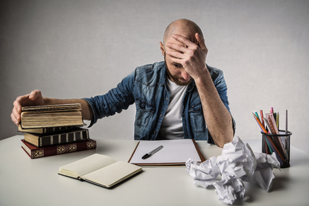 Desperate man sitting at a desk with booksの写真素材