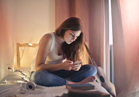 Girl with a smartphone on her bedの写真素材