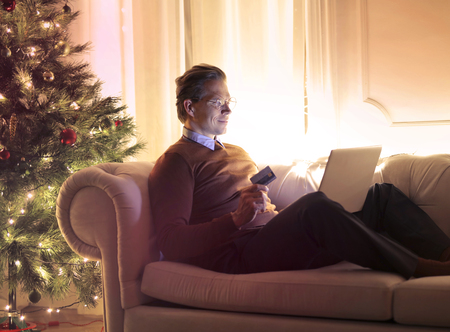 Man with a laptop and a card on a sofaの写真素材