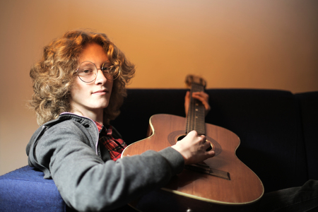 Guy playing acoustic guitar on a sofaの写真素材