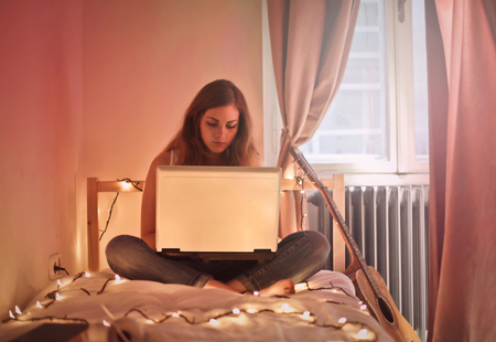 Girl sitting on a bed with a laptopの写真素材