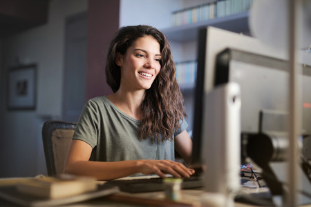 Smiling girl sitting at a desk with computerの写真素材