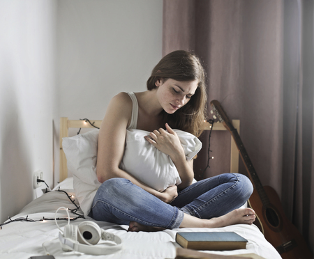 Sad girl on a bed hugging a pillowの写真素材