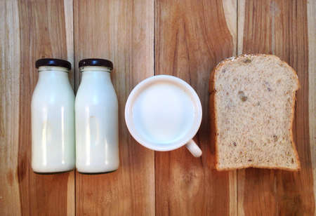 Slice of bread with bottle and cup of milk on wooden backgroundの写真素材
