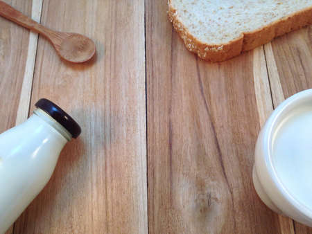 Slice of bread with bottle and cup of milk, wooden spoon on wooden backgroundの写真素材