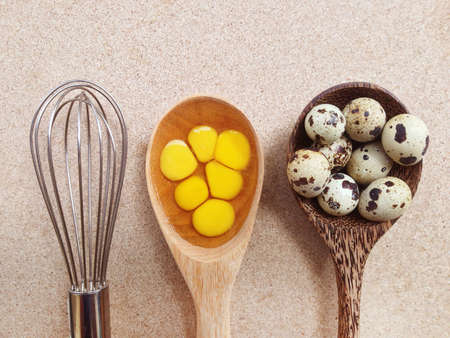 Quail eggs in wooden spoon and egg whisk on plywood backgroundの写真素材