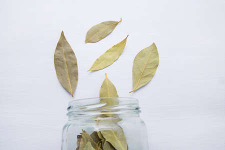 Dried bay leaves in glass jar on white wooden background.の写真素材