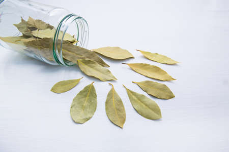 Dried bay leaves in glass jar on white wooden background.の写真素材