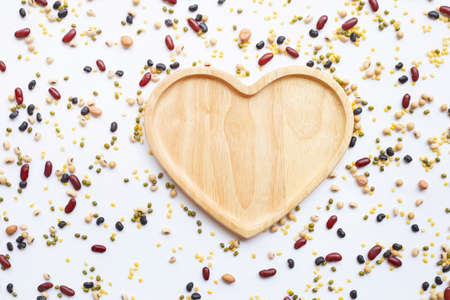 Top view of different legumes with empty wooden heart shaped plate isolated on white background.の写真素材